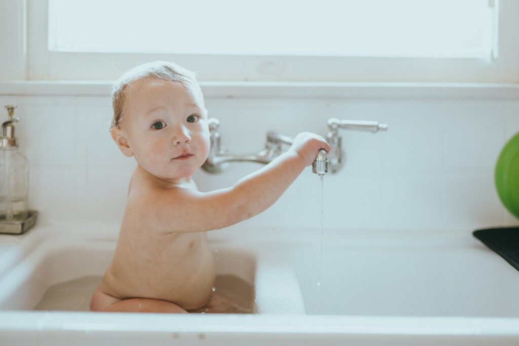 Baby baden in der Wanne: Kind sitzt fröhlich im körperwarmen Badewasser