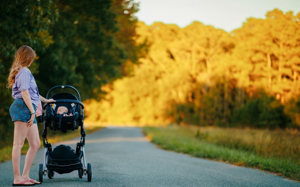 Frau schiebt einen Kinderwagen über eine Landstraße, ein wichtiger Teil der Erstausstattung Baby