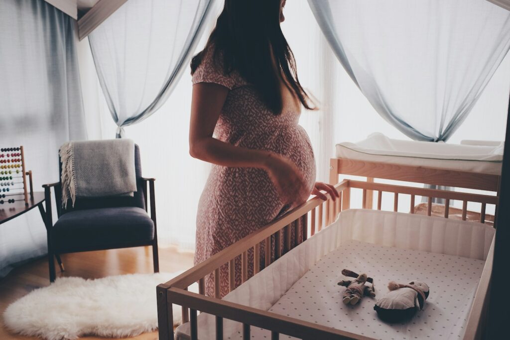 Schwangere Frau im Kinderzimmer vor dem Babybett – rechtzeitig die Kliniktasche packen