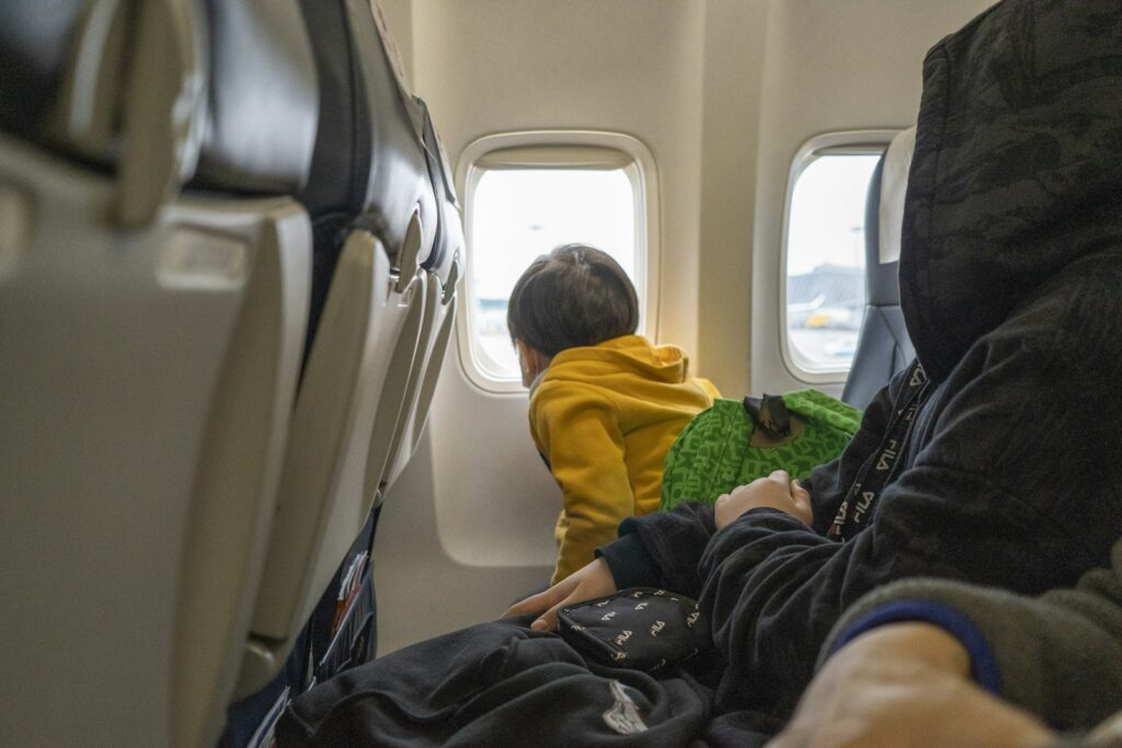 Kleinkind sitzt auf einem Flugzeugsitz am Fenster beim Reisen mit Baby