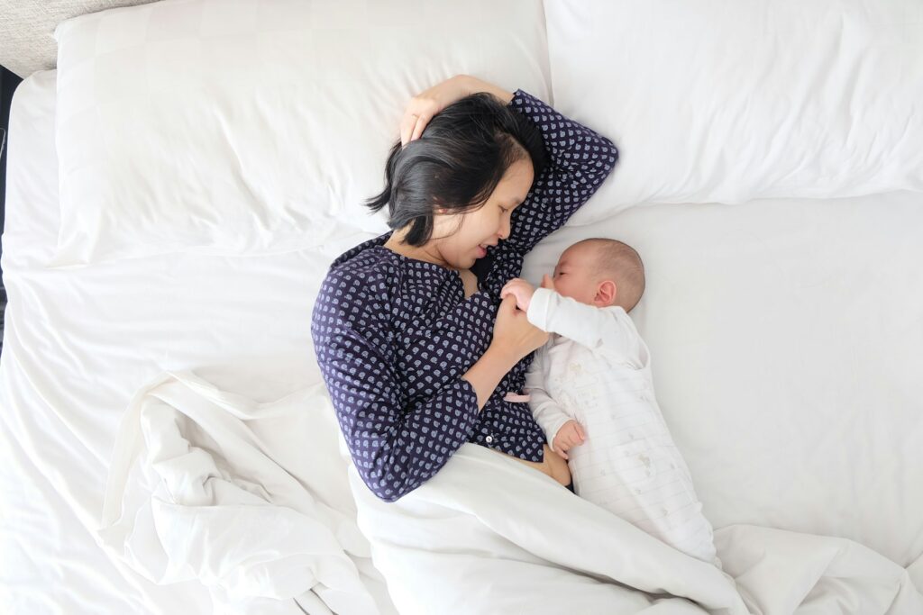 Mutter liegt mit ihrem Neugeborenen im Bett und erholt sich im Wochenbett